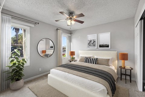 A bedroom with a large bed, a ceiling fan, and a mirror on the wall.