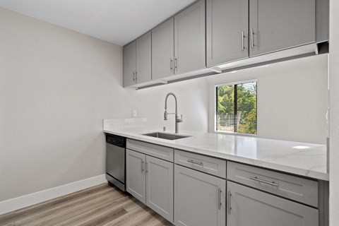 A kitchen with a white counter top and grey cabinets.