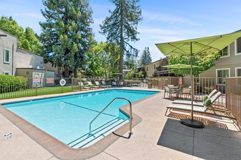 A swimming pool surrounded by trees and chairs under a yellow umbrella.
