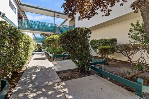 A green bench is situated in a courtyard with a concrete floor and a white wall.