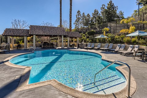 A large outdoor swimming pool surrounded by sun loungers and umbrellas.