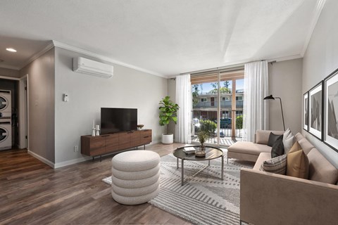 A living room with a brown sofa, a white ottoman, and a wooden floor.
