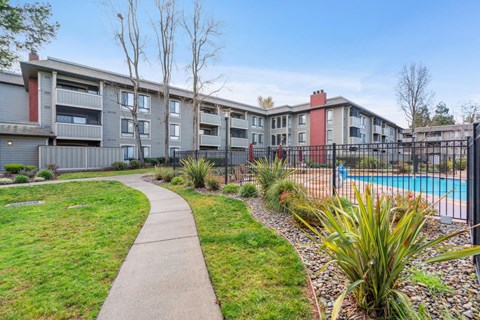 A pool is surrounded by a fence and a grassy area with a walkway.