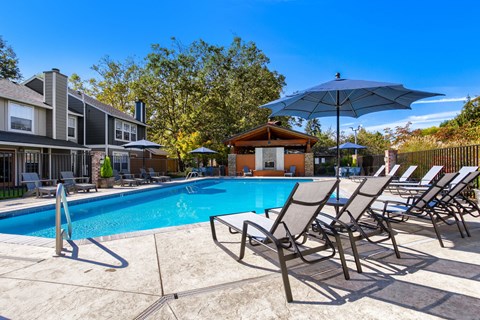 A pool surrounded by chairs and umbrellas with a building in the background.