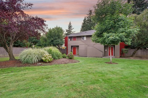 A house with a red door is surrounded by a green lawn and trees.