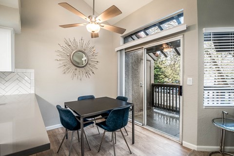 A dining room with a table and chairs and a fan on the wall.