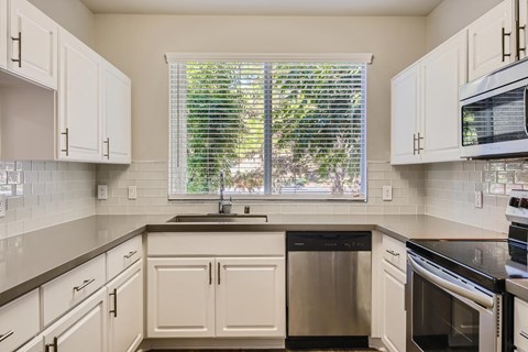 A kitchen with white cabinets and a window with blinds.
