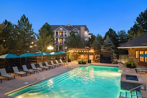 A large swimming pool surrounded by lounge chairs and umbrellas in front of a large house.