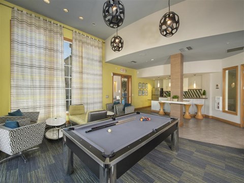 A pool table is in the middle of a room with a yellow wall and a window with yellow curtains.