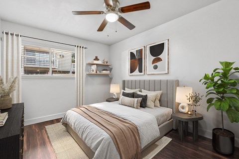 A bedroom with a bed, a ceiling fan, and a potted plant.