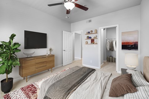 A bedroom with a bed, a ceiling fan, and a cabinet with a TV on the wall.