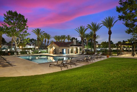 a swimming pool with chairs and a house at dusk