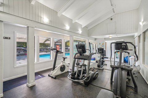 A gym with a row of treadmilers and elliptical machines.