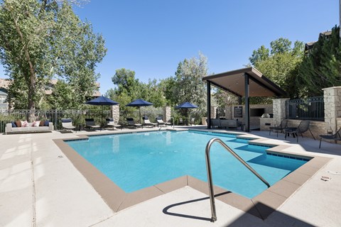 A large outdoor swimming pool surrounded by a patio with chairs and umbrellas.