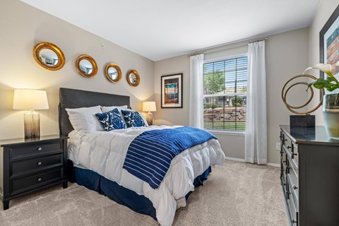 A bedroom with a large bed and a window with white curtains.