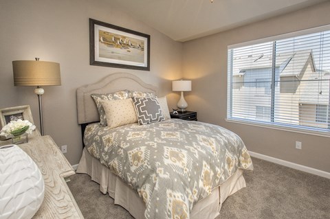 A bedroom with a bed, two lamps, and a painting on the wall.