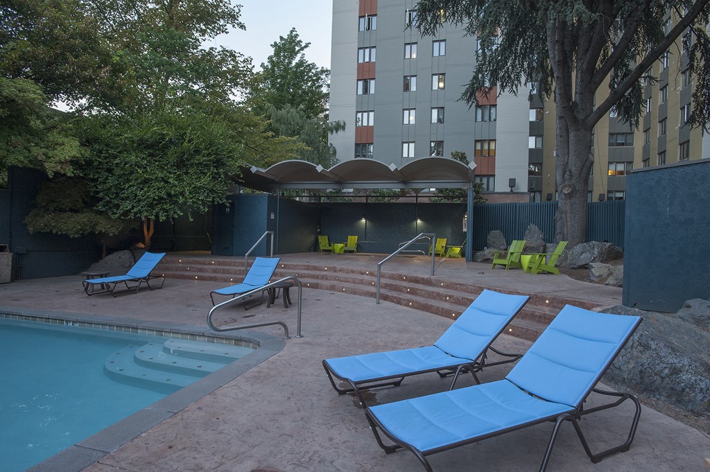 an empty pool with blue lounge chairs in front of a building