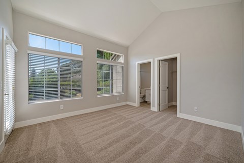 A room with carpeted floor and two windows with blinds.