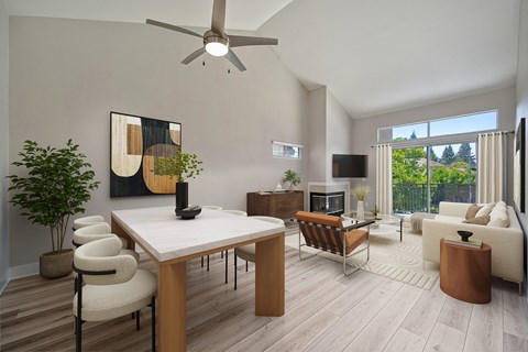 A modern living room with a white table and chairs, a brown leather ottoman, and a ceiling fan.