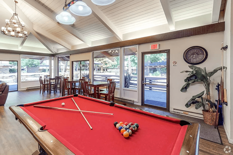 A pool table with a red cloth and a white cue stick.