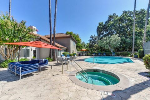 A pool area with a hot tub and a patio with chairs and a table.