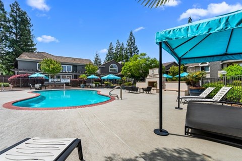 A pool area with a blue umbrella and a white bench.