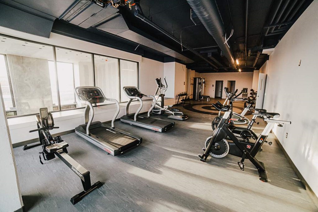 a gym with cardio equipment in a room with windows