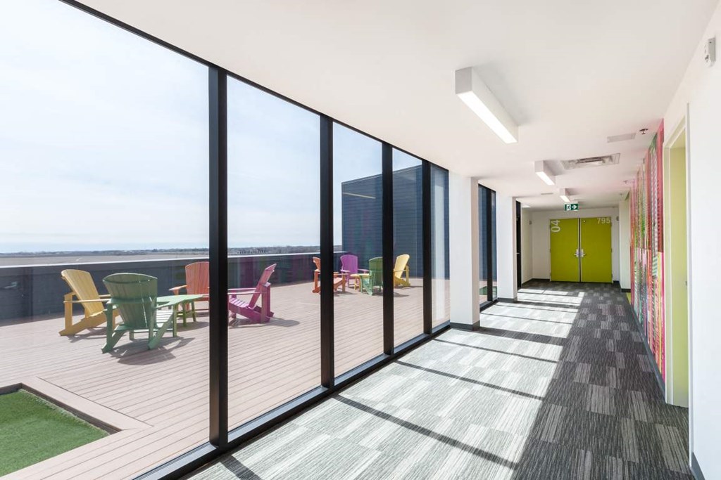 a long corridor with large windows and a patio with chairs and tables