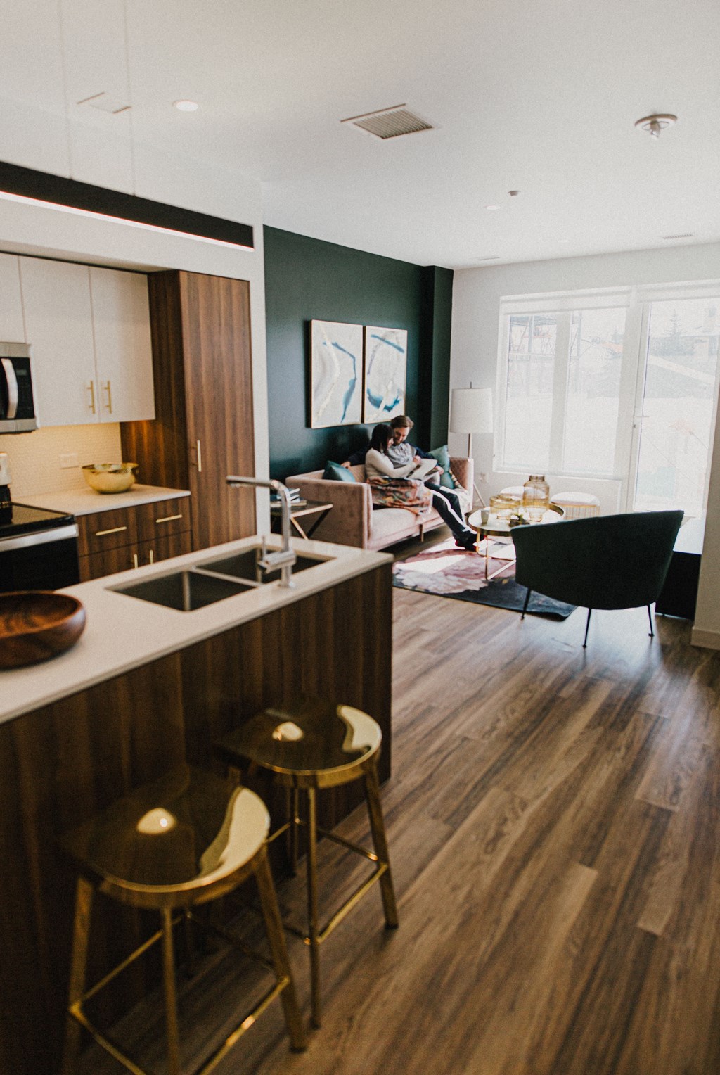 a living room and kitchen with a woman sitting on a couch