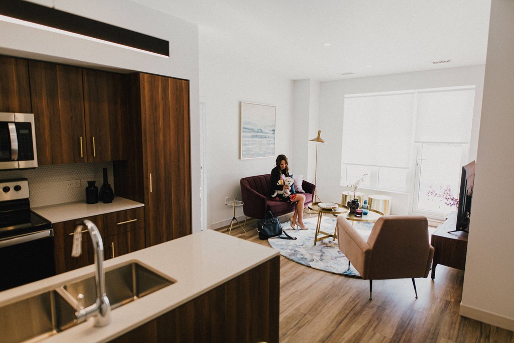 A woman is sitting on a couch in a modern kitchen with wooden cabinets and a stove.
