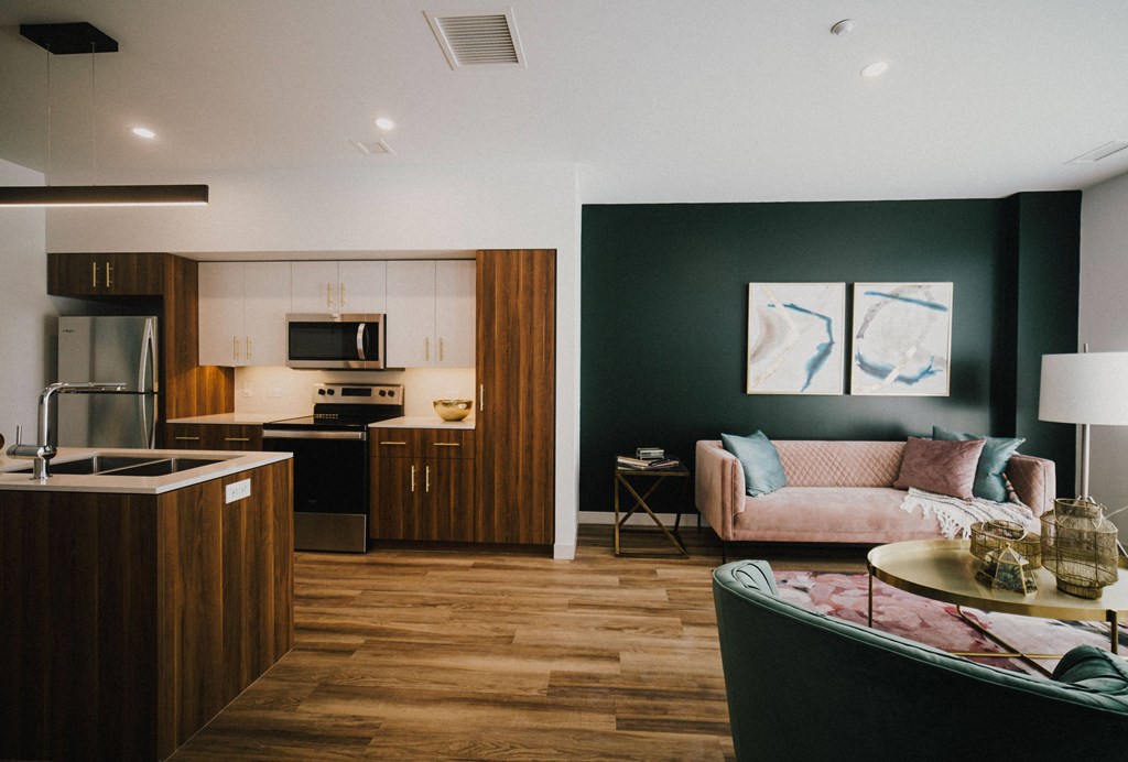 A modern kitchen with dark wood floors and a pink sofa in the living room.