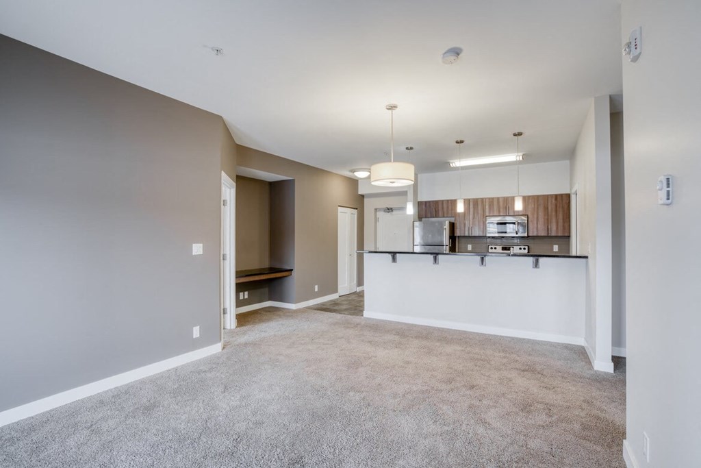 an empty living room with a kitchen in the background