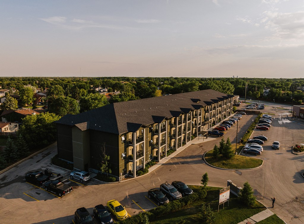 an aerial view of a large building with a parking lot and trees in the background