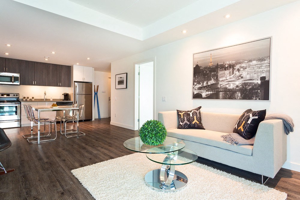 a living room with a couch table and chairs and a kitchen in the background