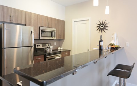 A kitchen with a black counter top and stainless steel appliances.