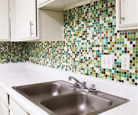 A kitchen with a white sink and a tiled wall.