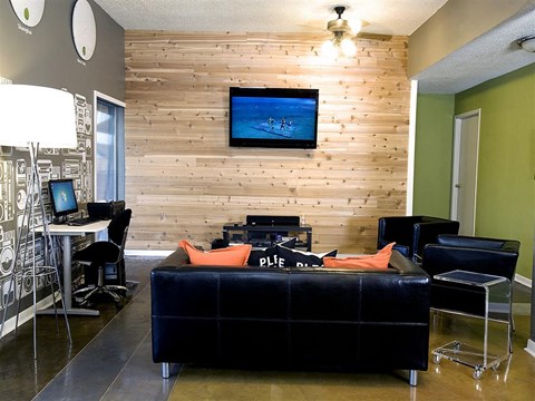 A living room with a black couch and a flat screen TV mounted on a wooden wall.