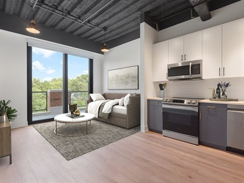 A modern kitchen with a stainless steel oven and microwave, a grey countertop, and a living area with a sofa and coffee table.
