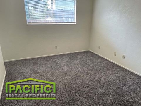 a carpeted room with a window and pacific rental properties logo on the floor