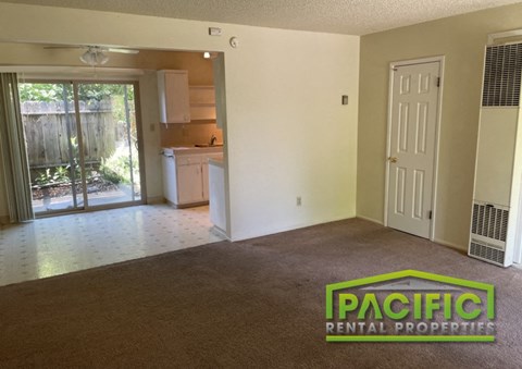 an empty living room with a door to a kitchen