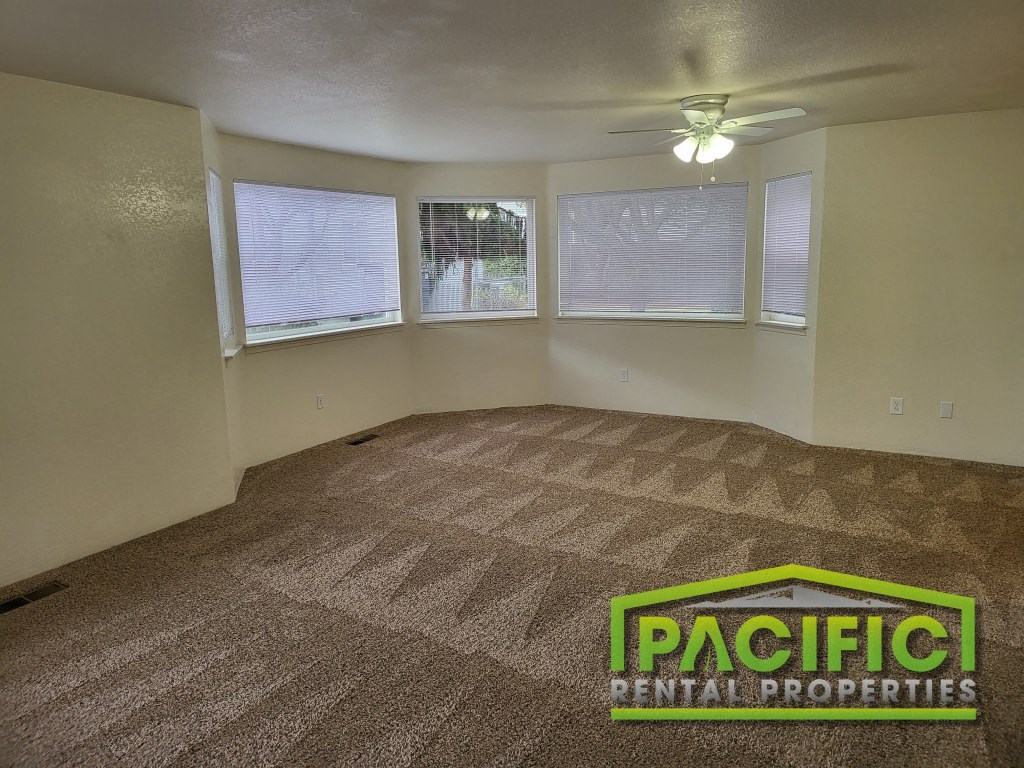an empty living room with a ceiling fan and three windows