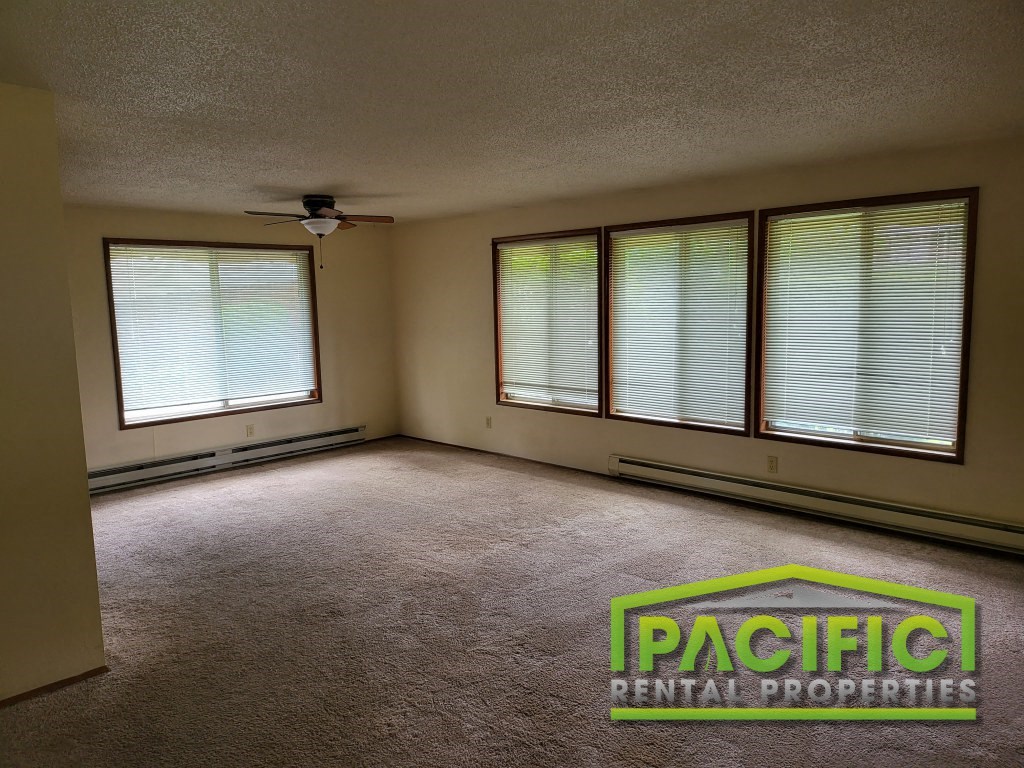 an empty living room with a ceiling fan and three windows