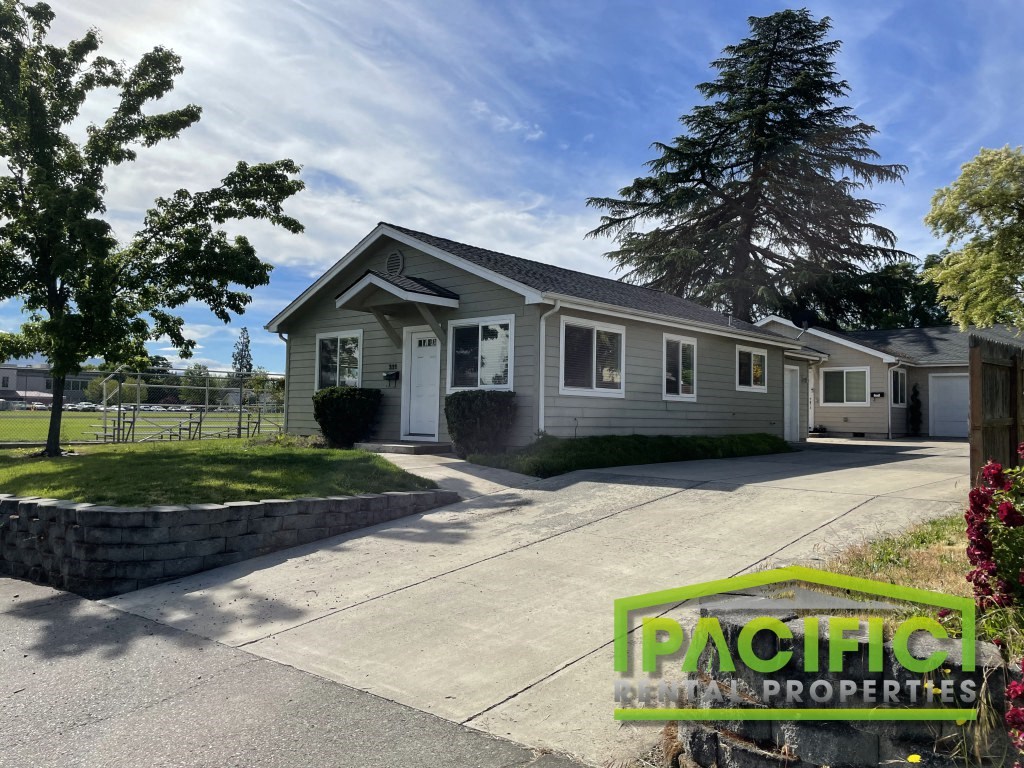 a small gray house with a driveway and a tree
