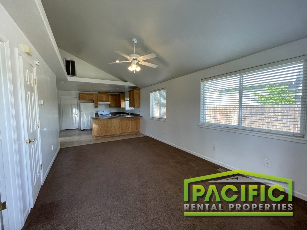 an empty living room with a ceiling fan and a kitchen