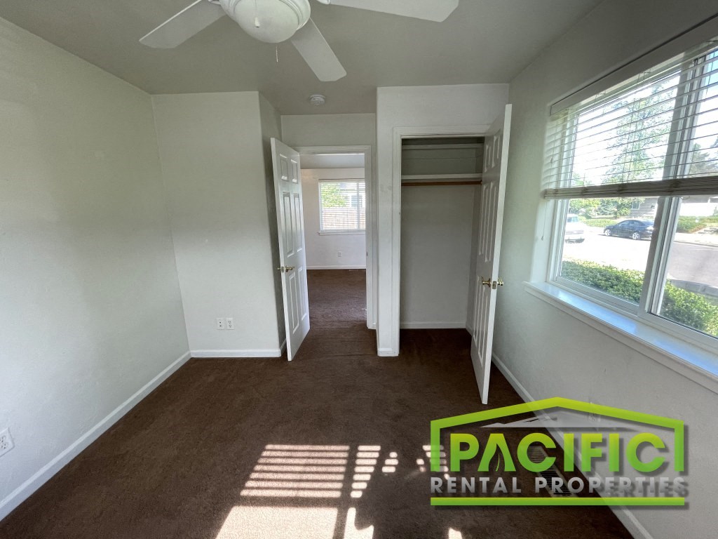 an empty room with a hallway to a closet and a ceiling fan