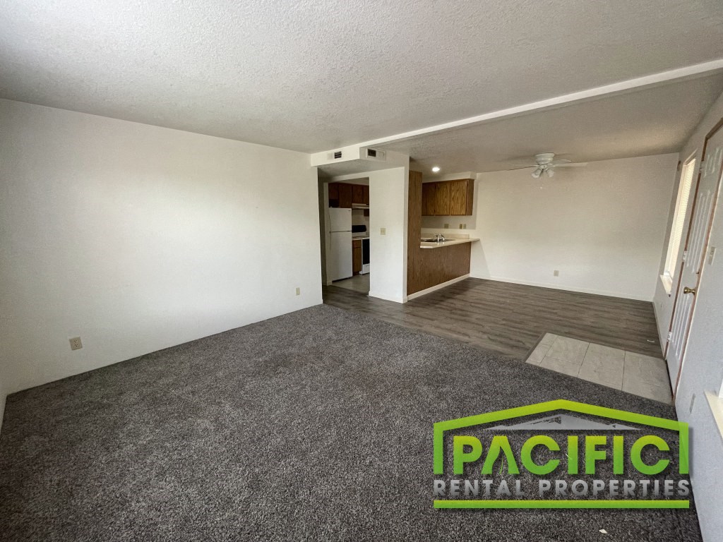 an empty living room with carpet and a kitchen