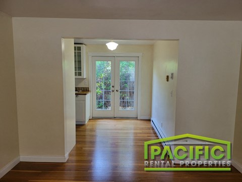 an empty living room with a hard wood floor and a door into a kitchen