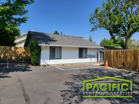 a small white house in a parking lot with a fence