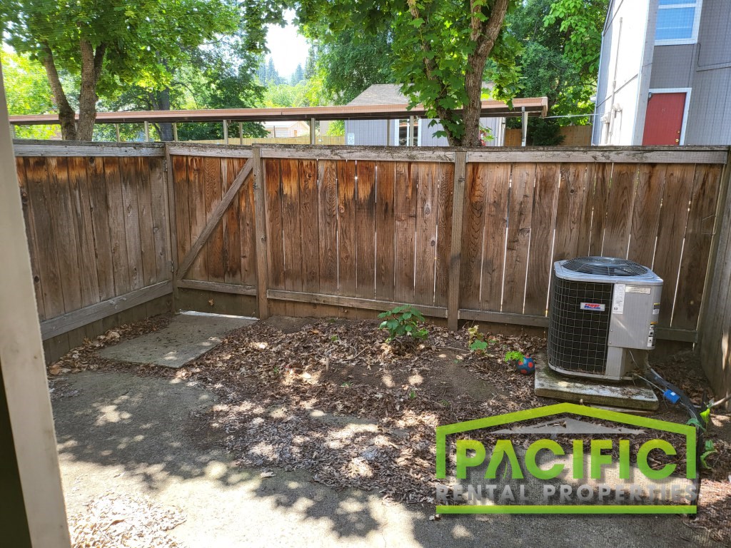 a backyard with a wooden fence and a trash can