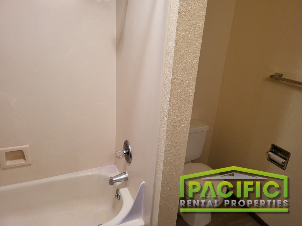 a bathroom with a tub and a toilet and a pacific rental properties sign
